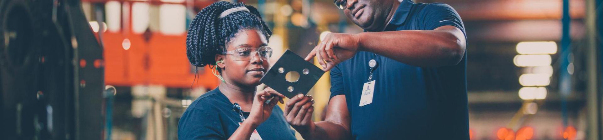 Two industrial workers looking at holes cut in a sheet metal plate