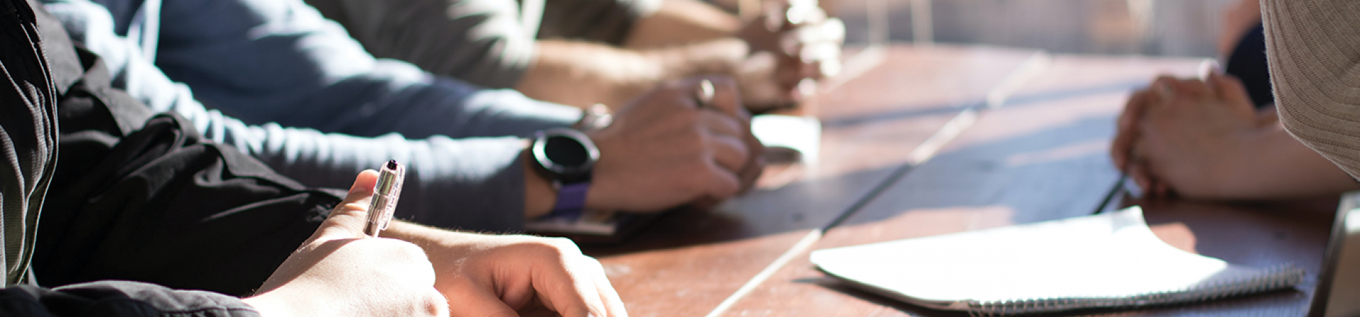 Peoples arms and hands with writing utensils and papers at a board room table