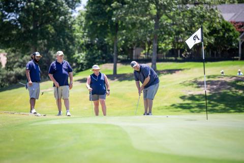 Golf player watching his ball roll toward hole with other teammates watching