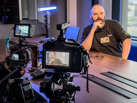 Crew member sitting at table as a stand-in for lighting with two cameras focused on him.