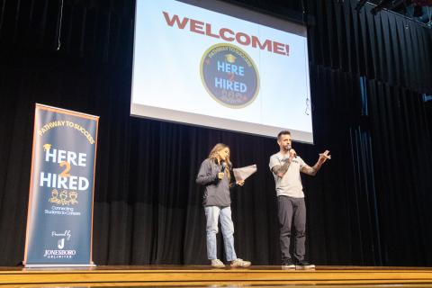 Chris Hughes and Bethania-Baray Harrison on stage at the kick off event with Here2Hired banner to left and above them
