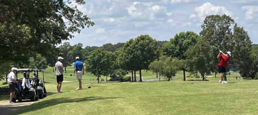 Golf player swinging club as others watch him