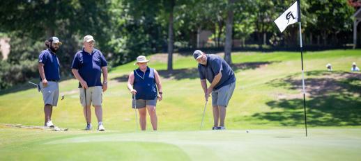 Golf player watching his ball roll toward hole with other teammates watching