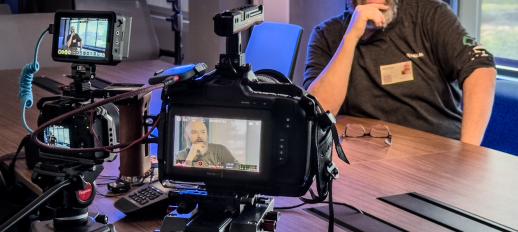 Crew member sitting at table as a stand-in for lighting with two cameras focused on him.